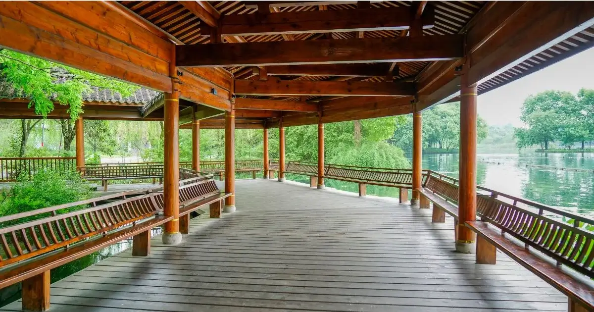 Covered timber pavilion with seating beside a peaceful lake.